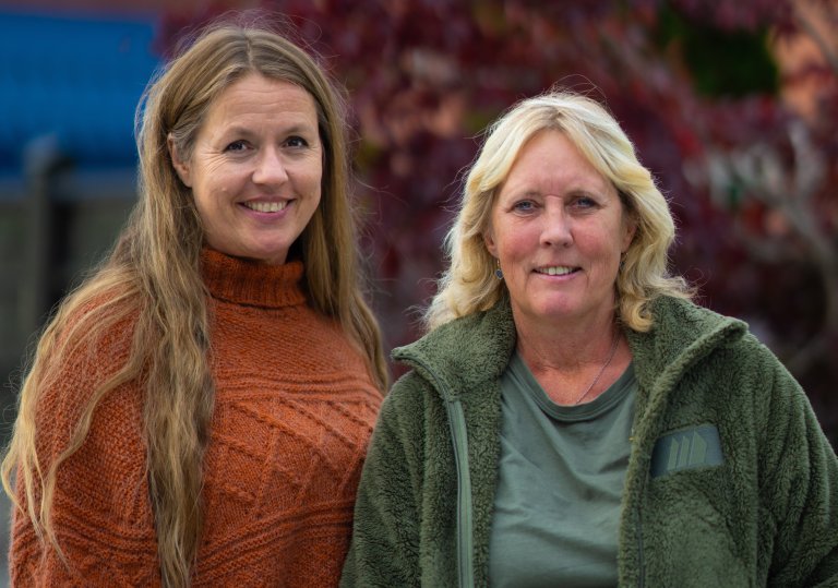 Bilde av to kvinner. Hun til venstre har rustrød genser og langt mellomblondt hår. Damen til høyre har på en grønn fleecegenser og blondt hår. Begge ser i kamera. Foto.